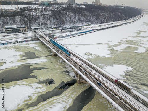 One train on Kiev metro bridge across the frozen Dnieper river. Textured pattern on ice. Aerial drone view. Winter snowy morning.