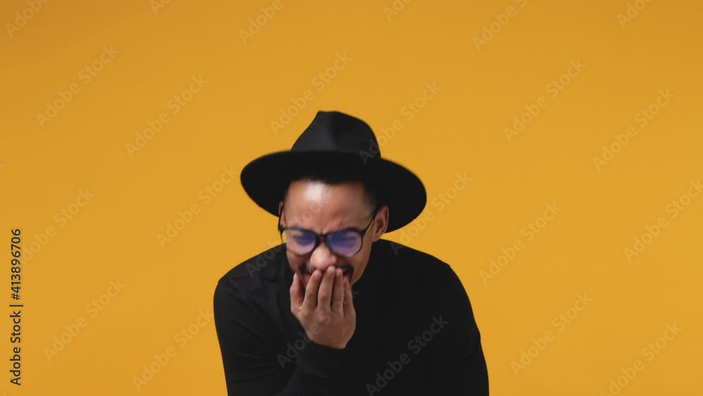 Laughing excited young african american man 20s in casual black clothes hat eyeglasses isolated on bright yellow color background in studio. People lifestyle concept. Point index finger camera on you Laughing excited young african american man 20s in casual black clothes hat eyeglasses isolated on bright yellow color background in studio. People lifestyle concept. Point index finger camera on you