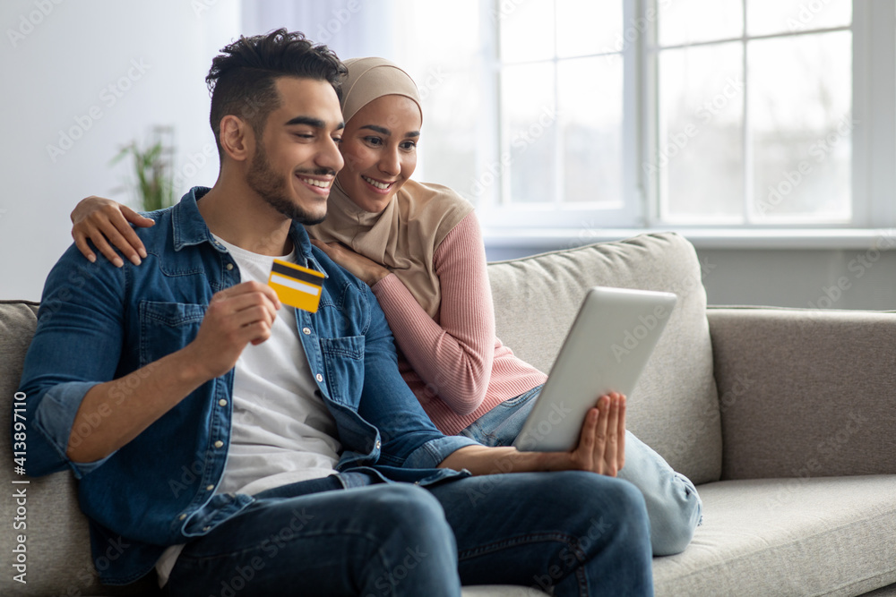 Smiling muslim couple with digital tablet and credit card