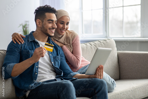 Smiling muslim couple with digital tablet and credit card