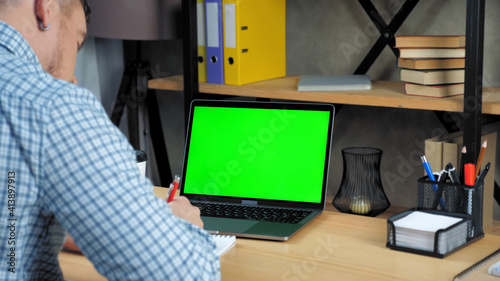 Green screen display laptop computer concept: Businessman at home office sitting on chair at desk writes information in notebook. Online remote distance business meeting webcam video conference call © viacheslav