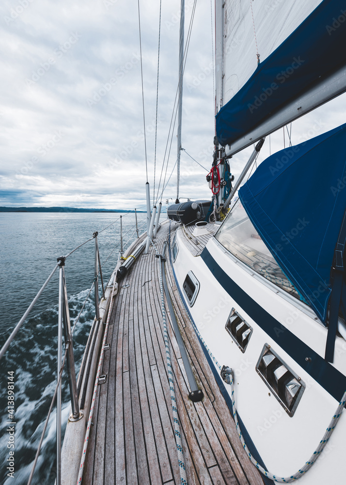 Sloop rigged modern yacht with wooden teak deck sailing near the rocky shore of Jura island on a cloudy day, close-up. Inner Hebrides, Scotland, UK. Sport, recreation, cruise, travel destinations - obrazy, fototapety, plakaty 