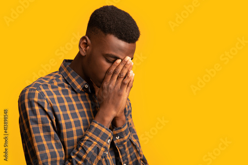 Upset black guy covering face with two hands in despair