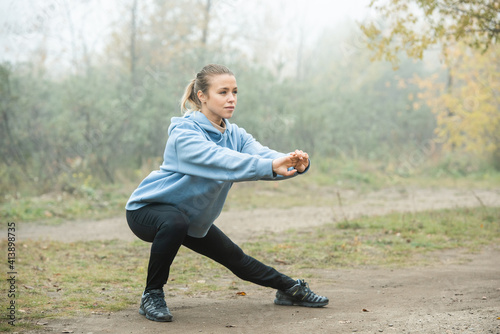 Active girl in blue hoodie, black leggins and sneakers doing exercise for legs