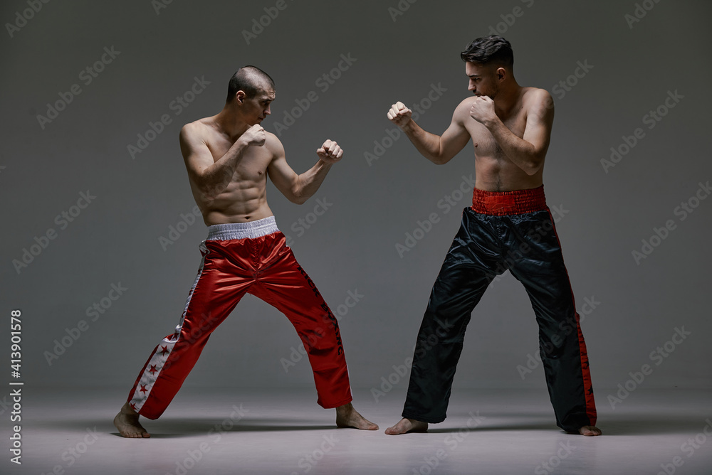 Boxers athletic guys fighting on gray studio background during kickboxing workout, mixed fight concept