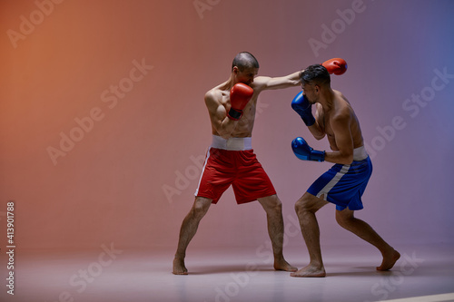 Sparring of fighting males boxers punching during battle on red blue studio backdrop, martial arts, mixed fight workout © Georgii