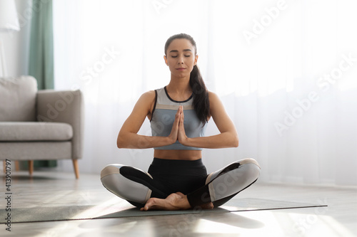 Peaceful sporty lady meditating at home, sitting in lotus asana