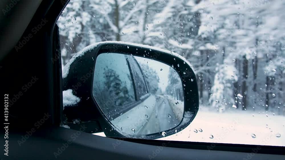 Car driving on snow covered road through winter snowy forest. View from side mirror.