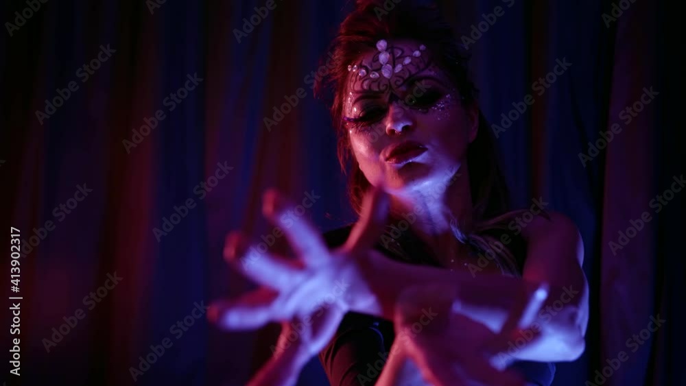 A beautiful passionate woman dances, makes swings of her head and hair while in the room against the background of blue curtains. She has a beautiful makeup with rhinestones. A beautiful passionate woman dances, makes swings of her head and hair while in the room against the background of blue curtains. She has a beautiful makeup with rhinestones.