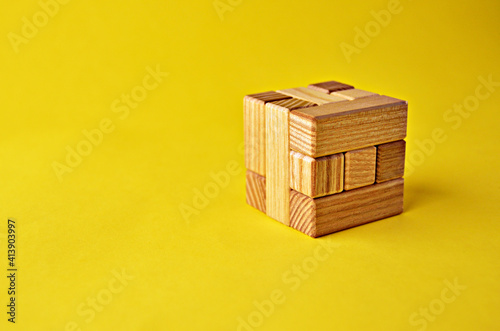 Logical puzzle game wooden cube puzzle in collected form on a yellow background with copy space. Solving logical problems. High quality photo