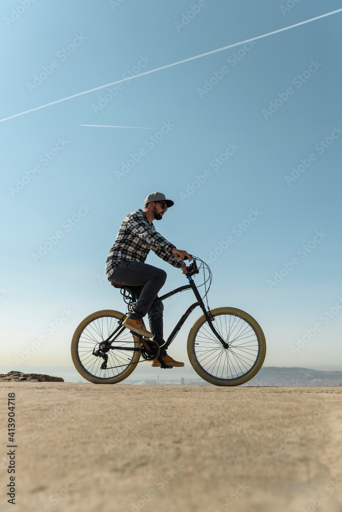 Surface level image of man riding bicycle on retaining wall against blue sky during sunny day