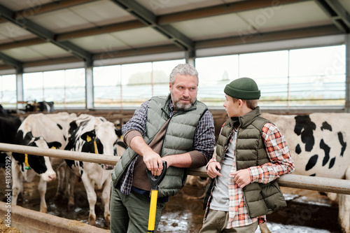 Mature grey-haired owner of animal farm talking to teenage boy by large paddock