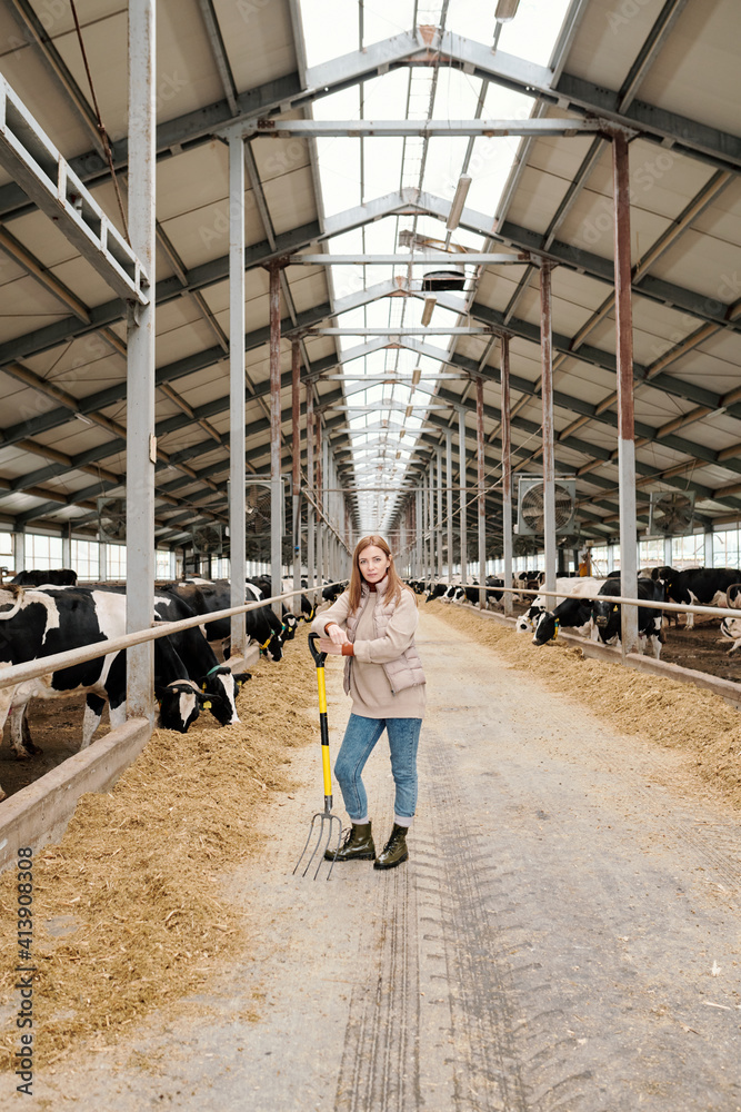 Young female worker of large contemporary animal farm standing in aisle