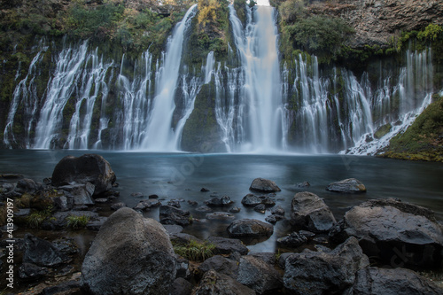 Burney Falls in early dawn light with stones in the foreground.