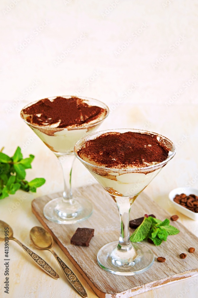 Tiramisu, dessert with biscuit cookies and mascarpone cream in triangular glasses on a light concrete background. Dessert recipes without baking. Desserts in glasses. Tiramisu, dessert with biscuit cookies and mascarpone cream in triangular glasses on a light concrete background. Dessert recipes without baking. Desserts in glasses.