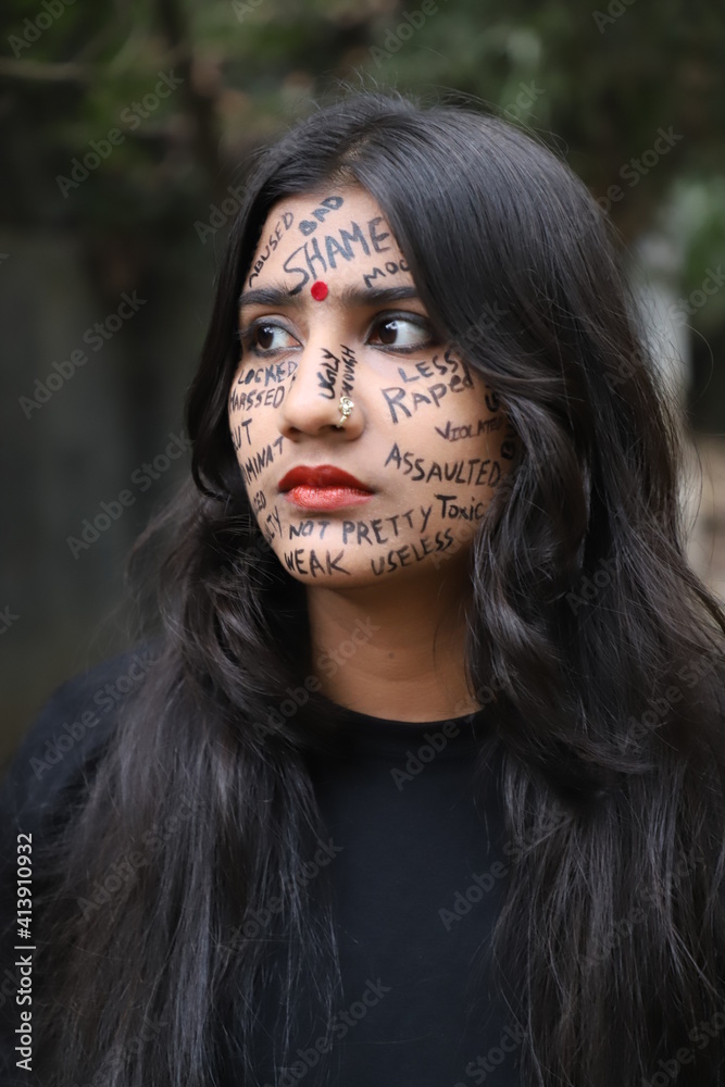 A southeast Asian brown woman protesting gender based violence by writing anti violence against women and girls messages all over her face