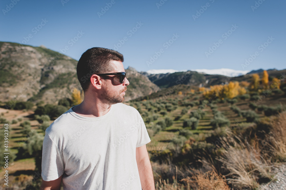 Young man in sunglasses looking at olive trees and snowy mountain Young man in sunglasses looking at olive trees and snowy mountain
