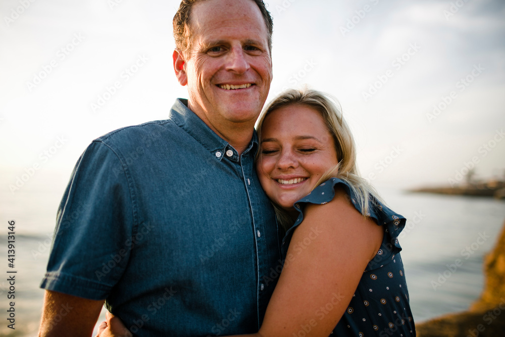 Portrait of happy father being embraced by daughter while standing on cliff against sea during sunset Portrait of happy father being embraced by daughter while standing on cliff against sea during sunset