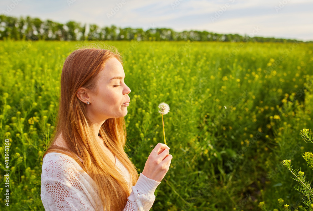 Young spring fashion redhead woman blowing dandelion in spring garden. Springtime, summertime. Trendy girl in summer landscape background. Allergic to pollen of flowers. Young spring fashion redhead woman blowing dandelion in spring garden. Springtime, summertime. Trendy girl in summer landscape background. Allergic to pollen of flowers.