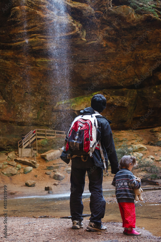 A father stands with his small daughter by a waterfall in sunlit gorge A father stands with his small daughter by a waterfall in sunlit gorge