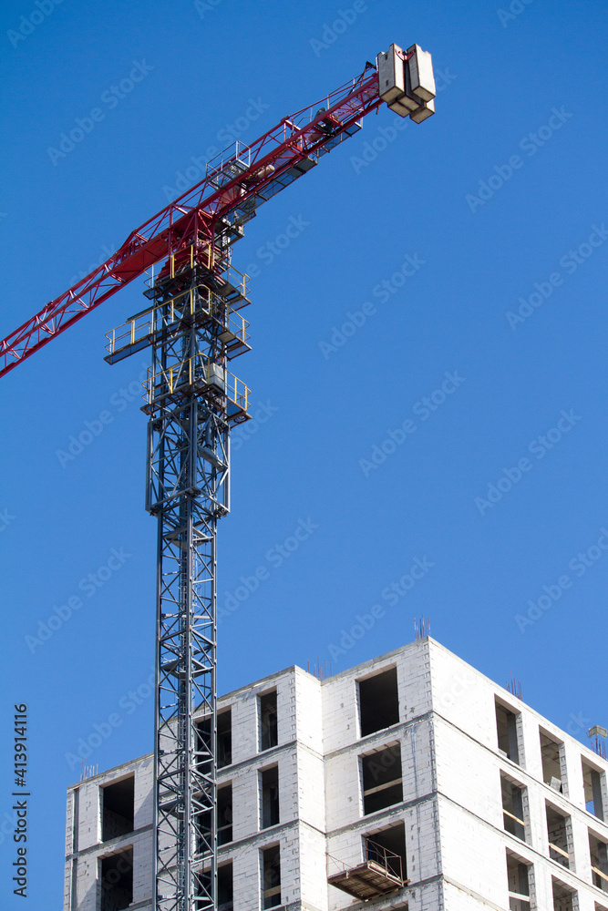 Blue and red tower crane near new building over blue sky, selective focus Blue and red tower crane near new building over blue sky, selective focus