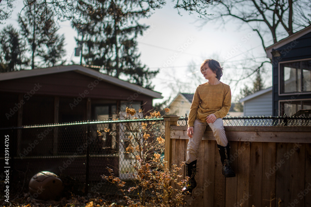 Portrait of a thoughtful child sitting on a yard fence in golden light Portrait of a thoughtful child sitting on a yard fence in golden light