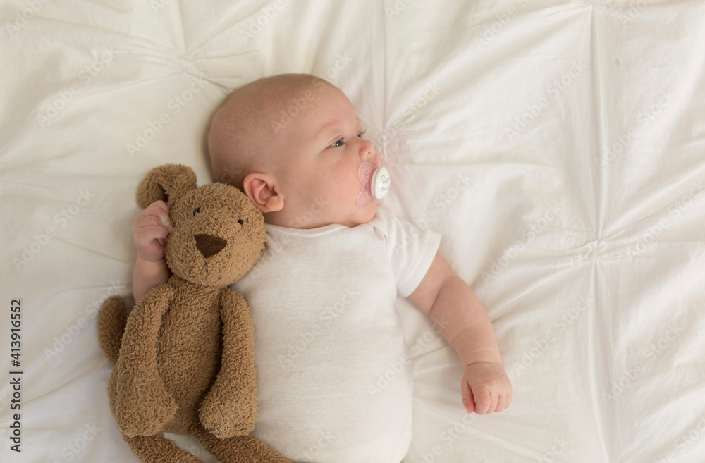 Overhead view of cute baby girl sucking pacifier while lying by teddy bear on bed at home Overhead view of cute baby girl sucking pacifier while lying by teddy bear on bed at home