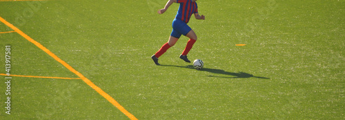 Jogador a correr isolado com a bola na direção da baliza na entrada da grande área - campo de treinos com relva artificial - equipamento em cores azul e vermelho