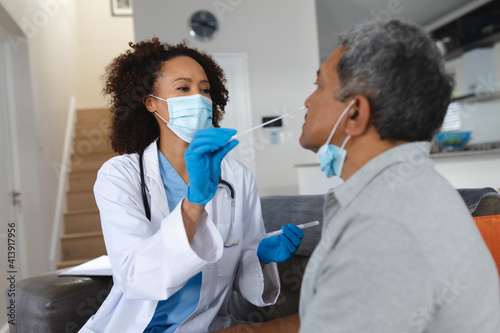 Senior mixed race man with female doctor home visiting wearing face masks taking swab test photo