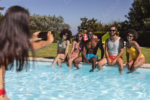 Diverse group of friends taking photo and sitting at the poolside