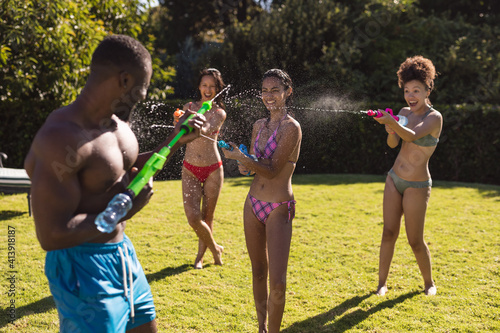 Diverse group of friends having fun playing with water guns at a pool party
