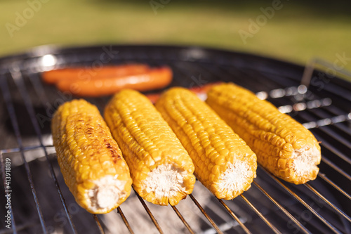 Close up of fresh grilled corns and tasty sausages on barbecue