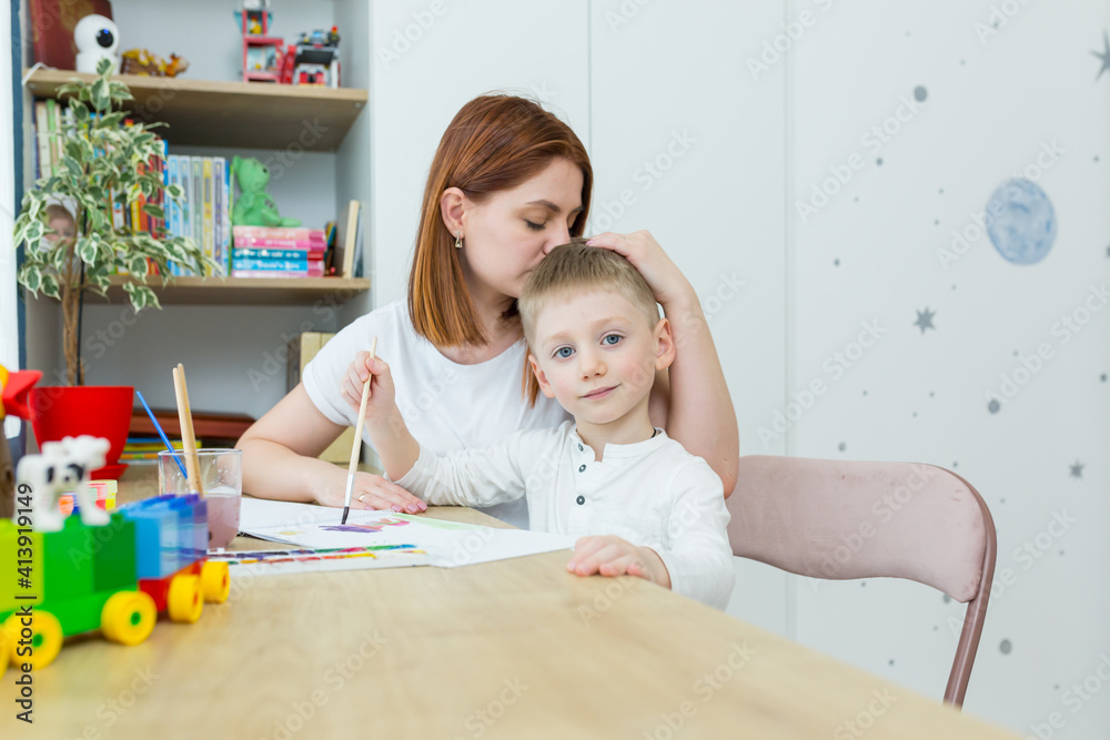 young mother draws teaches her little son to draw, in the nursery at home, having fun together
