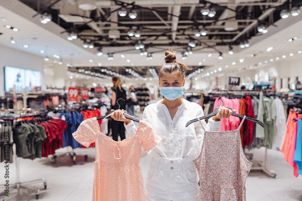 Young woman shopping apparels in clothing boutique with protective face mask