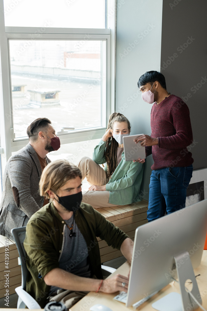 Three designers or managers in protective masks discussing online information Three designers or managers in protective masks discussing online information