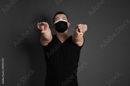 double mask. a young man, pointing with his forefingers forward, wearing a black T-shirt, against a dark background, wearing two disposable medical masks at the same time. © Alexandr