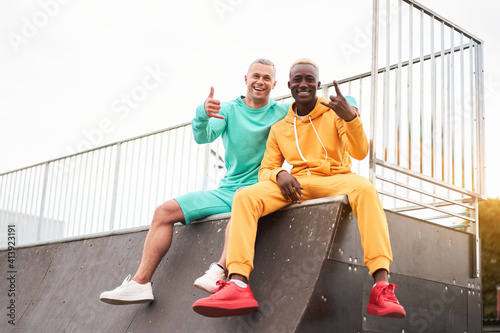 Multi-ethnic friendship Black african-american and caucasian guy friends spending time together on skate park Two multi ethnic student Dressed colorful sportswear.