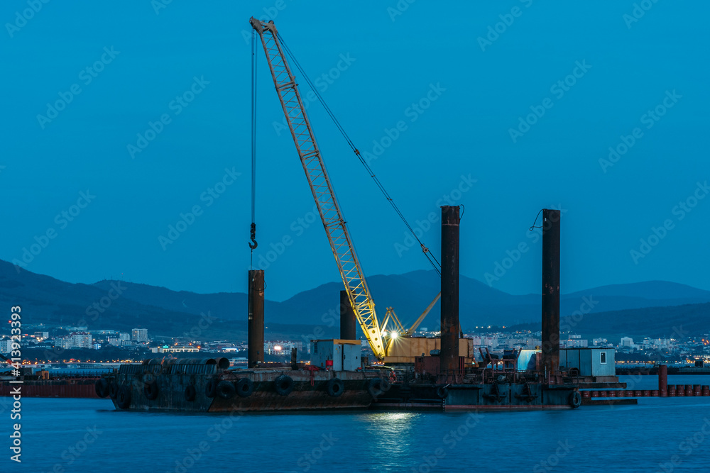 Cargo crane working in small port, construction of industrial harbor or dock in evening, sea goods transportation and logistic development concept.