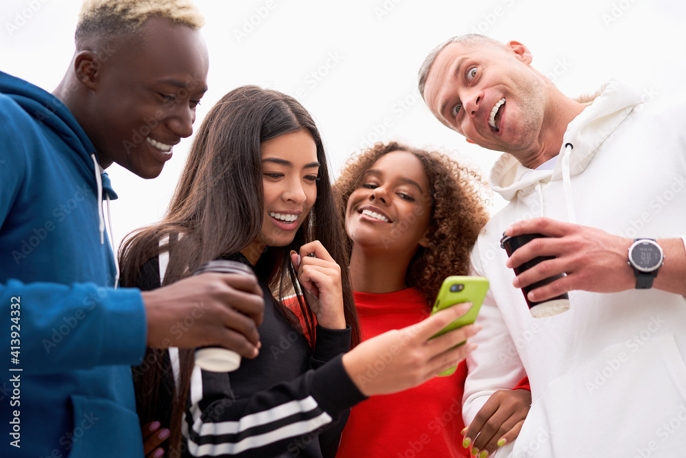 Fototapeta premium Multi-ethnic group teenage friends looking smartphone screen. African-american asian caucasian student spending time together Multiracial friendship Smiling People colorful sportswear drink coffee