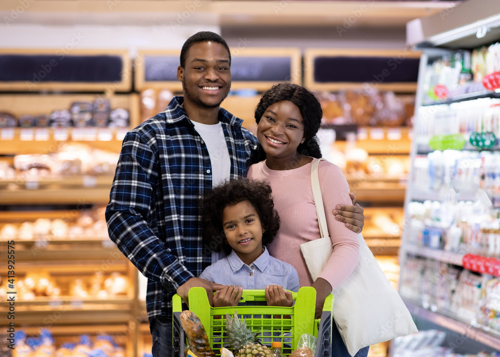 Portrait of smiling black parents with their daughter purchasing groceries at big supermarket