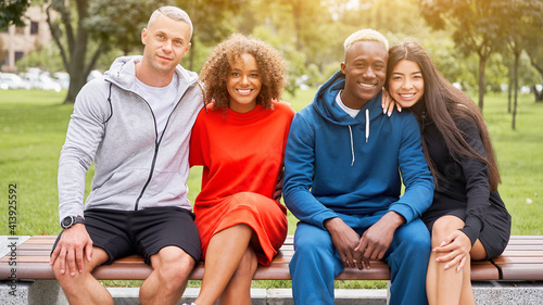 Multi-ethnic group teenage friends. African-american asian caucasian student spending time together Multiracial friendship Happy smiling People dressed colorful sportswear sitting bench park outdoor © Andrii