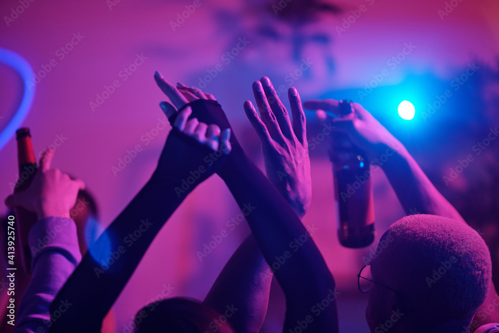 Raised arms of young excited intercultural friends dancing at home party