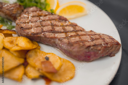 Pepper or mustard steak, grilled on a plate and served with some baked potatoes on a plate in a restaurant. Delicious meal served on a white plate.