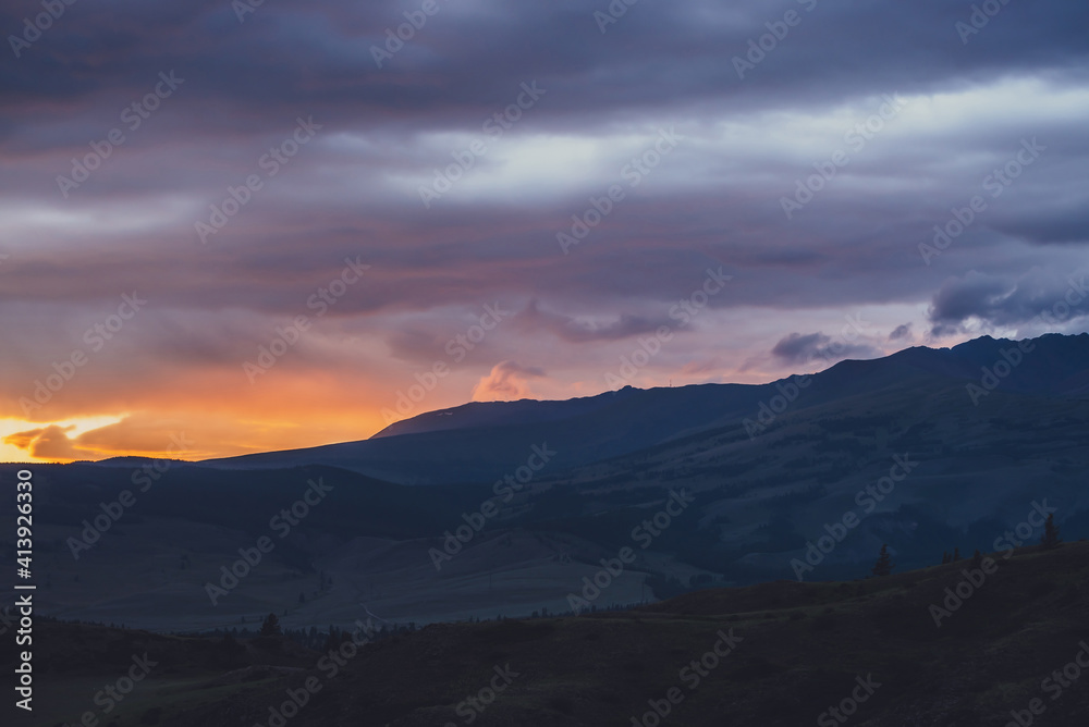 Atmospheric landscape with silhouettes of mountains with trees on background of vivid orange blue violet dawn sky. Colorful nature scenery with sunset or sunrise of illuminating color. Sundown paysage
