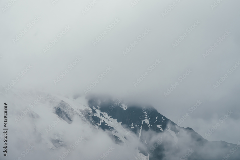 Minimalist monochrome atmospheric mountains landscape with big snowy mountain range in low clouds. Awesome minimal scenery with glacier on rocks. Black white high mountain ridge with snow in clouds.