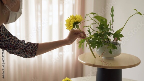 Mujer con mascarilla colocando un girasol en un jarrón de plantas