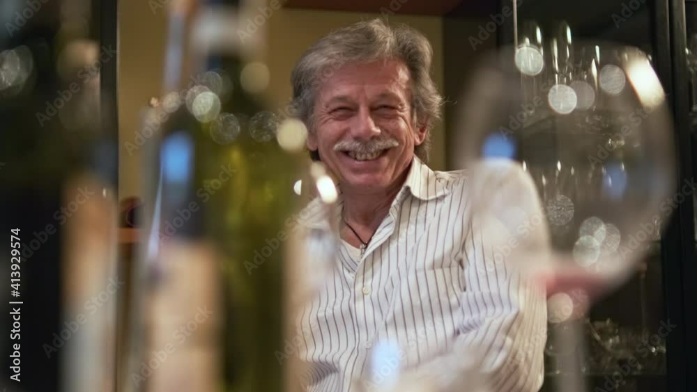 Happy Healthy Eldery Male at Family Gathering by Dining Table, Selective Focus. Red Wine Bottle and Glasses in Front, Slow Motion Happy Healthy Eldery Male at Family Gathering by Dining Table, Selective Focus. Red Wine Bottle and Glasses in Front, Slow Motion