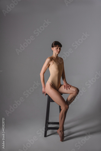 Attractive, slim, adult woman in a beige swimsuit on a gray background in the studio. The concept of a beautiful figure, body positive, healthy lifestyle