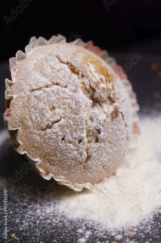 cupcake in powdered sugar on a plate on a black background