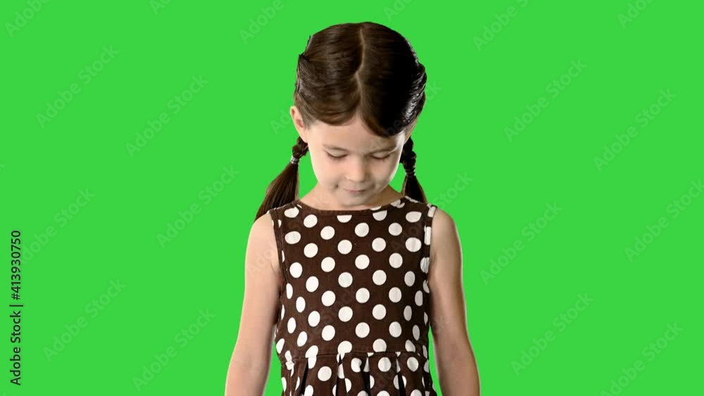 Smiling little girl in polka dot dress with pig tails walking to the camera looking down at her feet on a Green Screen, Chroma Key. Smiling little girl in polka dot dress with pig tails walking to the camera looking down at her feet on a Green Screen, Chroma Key.